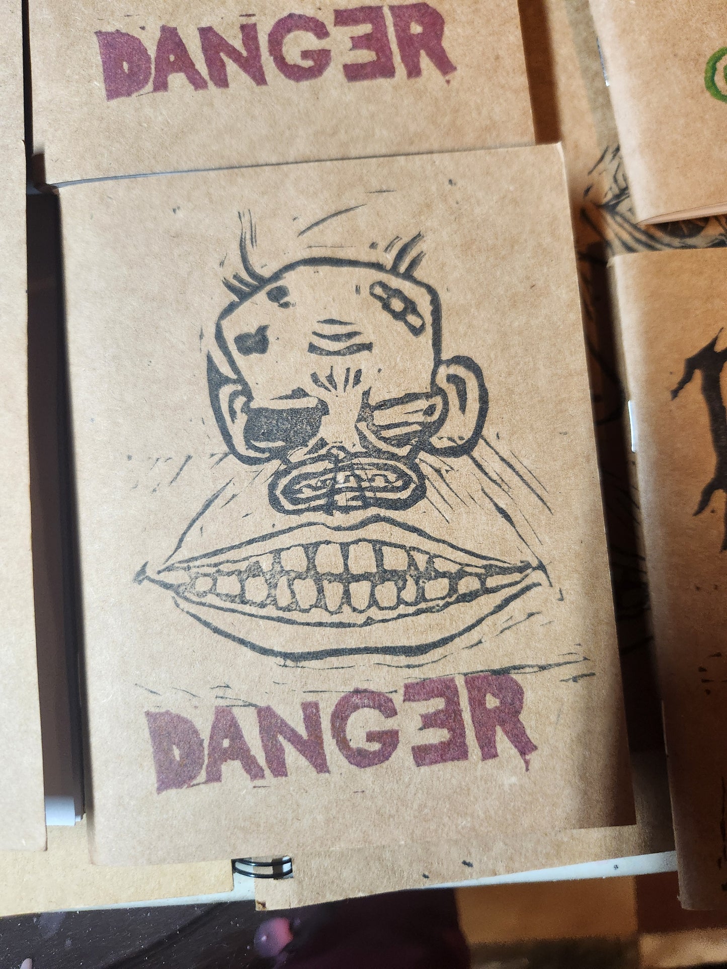 Close up of a stamped craft paper notebook. It features an angry cartoon monkey face, with an exaggerated mouth, and the word danger stamped below with a backwards E