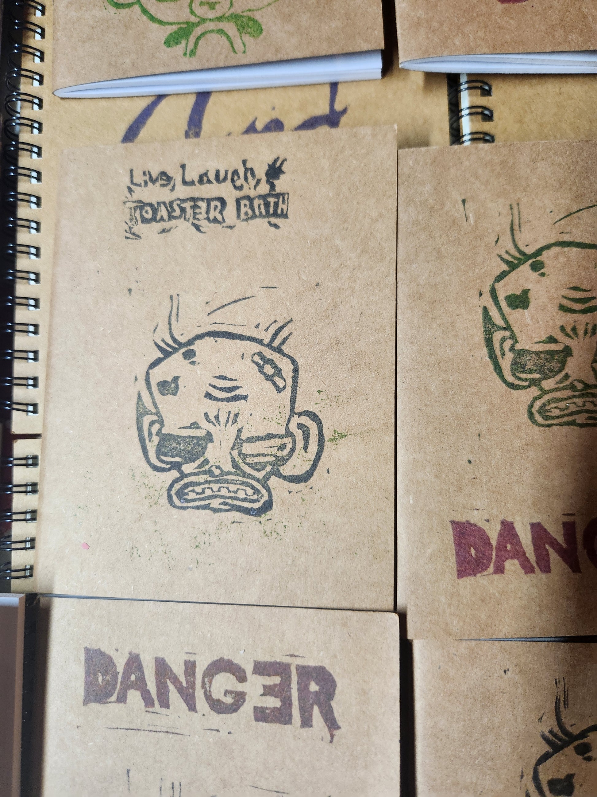 A Close up picture of the cover of a craft paper note book. Live, Laugh, Toaster Bath is written on top, with an angry cartoon monkey head below.